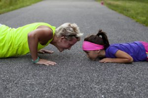 The picture of woman and little girl exercising on a walkway in the park.