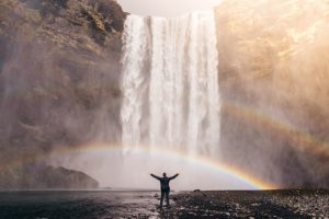 Health supplements. The colrful illustration of a man raising his hands into the air on the beach front of a fresh waterfall in front of a doubke rainbow.