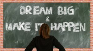 The picture of the chalkboard with a person in front of it, stating dream big and make it happen.