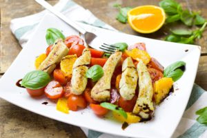 The picture of a very appetizing healthy plate of food, including grilled chicken strips, and fruits and veggies.