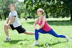 The picture of two people doing stretch exercise, is a park.