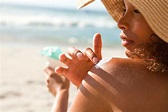 The picture of a woman at the beach putting sun screen on her shoulder.