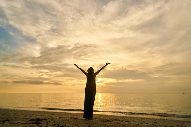 The picture of a woman holding her hands in the air on the beach during sunset.